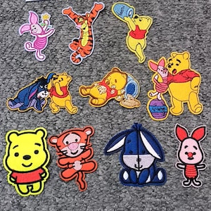 Può includere: Un set di dieci toppe da stirare con diversi personaggi dei cartoni animati della serie Winnie the Pooh. Le toppe sono colorate e presentano personaggi come Winnie the Pooh, Tigro, Maialino e Ih-Oh.