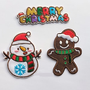 Pode incluir: Três patches bordados para passar a ferro que representam um boneco de neve, um homem de gengibre e a frase "Feliz Natal". O boneco de neve usa uma echarpe vermelha e verde e um chapéu vermelho. O homem de gengibre usa um chapéu vermelho e branco e uma echarpe verde. A frase "Feliz Natal" está em letras coloridas.