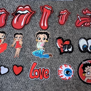 May include: Assortment of iron-on patches featuring cartoon characters, lips, eyes, and hearts.  The patches include Betty Boop, a red heart, a pair of eyes, and a red heart with a white centre.