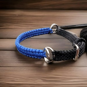 Puede incluir: Un collar de perro de paracord azul y negro con dos anillos de metal plateado. El collar está hecho de paracord trenzado.