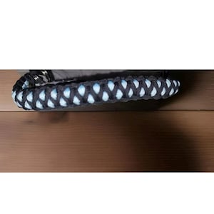 May include: Close-up of a black and light blue braided rope handle.