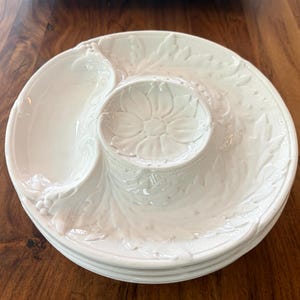 May include: White ceramic serving platter with a floral and leaf design. The platter has a central bowl and two curved sections, ideal for serving appetizers or snacks. The design is embossed and adds a touch of elegance.