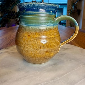 Puede incluir: Un juego de tres tazas de cerámica con un acabado moteado y mate. Las tazas son de color crema, gris claro y gris oscuro. Cada taza tiene un diseño simple y minimalista.