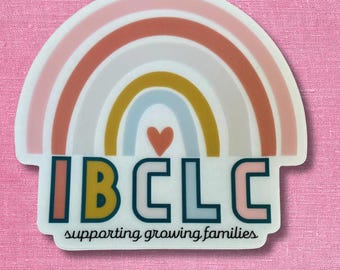 May include: A die-cut sticker featuring a pastel rainbow arch with a small heart in the centre. Below the rainbow, the text reads IBCLC in bold, colourful block letters, followed by the phrase supporting growing families in a black script font.