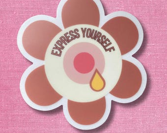 May include: A flower-shaped sticker with brown petals and a cream-colored center. The center features the text "EXPRESS YOURSELF" in brown letters, a solid pink circle, and a small yellow teardrop shape positioned below the pink circle.
