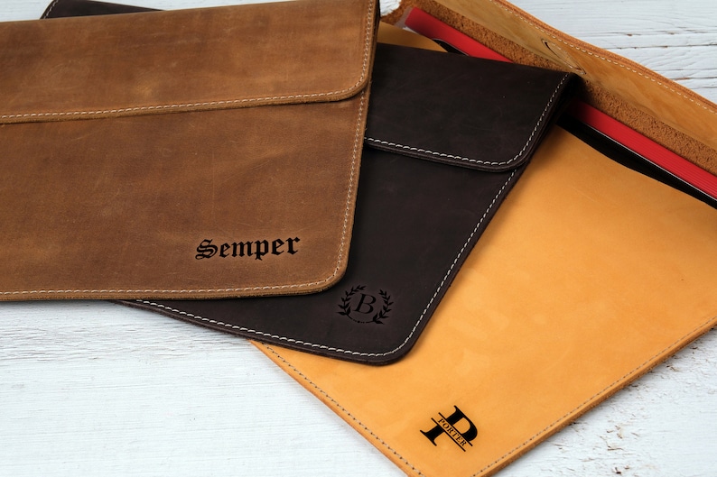 Pu&ograve; includere: Custodie per laptop in pelle nei toni del marrone e del beige, con cuciture bianche. Una custodia &egrave; impressa con la parola "Semper", un'altra con una "B" in una corona e una terza con la lettera "P" e il nome "Porter".