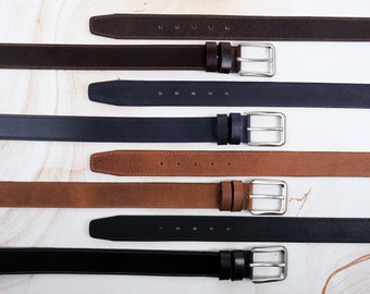 May include: A collection of four belts arranged horizontally. The set includes a dark brown suede belt, a navy blue leather belt, a tan suede belt, and a black leather belt. Each belt features a silver-toned metal buckle and two matching loops.