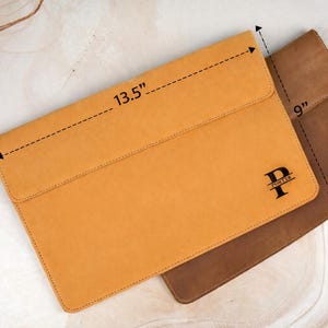 Pu&ograve; includere: Due custodie per laptop in pelle, una giallo senape e una marrone. La custodia gialla misura 34,3 cm di lunghezza e 22,9 cm di larghezza. La custodia gialla ha una chiusura a patta e una iniziale nera "P" con il nome "PORTER" sotto.