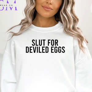 May include: White sweatshirt with the text "Slut for Deviled Eggs" printed in black.
