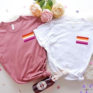 May include: Two t-shirts with the lesbian pride flag printed on the front. The t-shirts are in heather mauve and white.