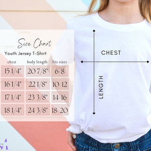 以下が含まれることがあります： 子供用ジャージTシャツのサイズ表。表には、YS、YM、YL、YXLのサイズと、それに対応する胸囲と胴体の長さのインチ単位の寸法が示されています。表には、各サイズに合う年齢層も示されています。