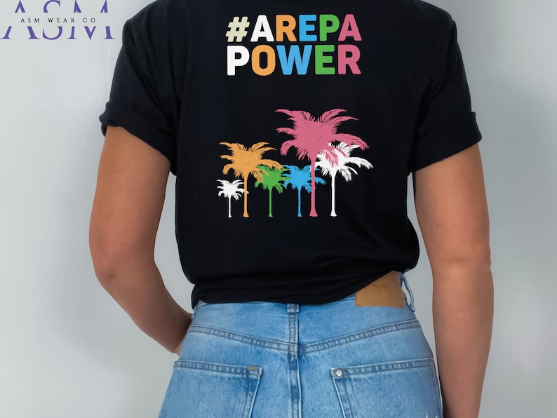 May include: Black t-shirt with the text "#AREPA POWER" in rainbow colors and a row of colorful palm trees below the text.