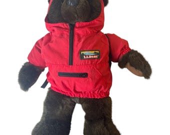 Chaqueta anorak impermeable vintage roja con oso de peluche marrón de LL Bean y mochila.