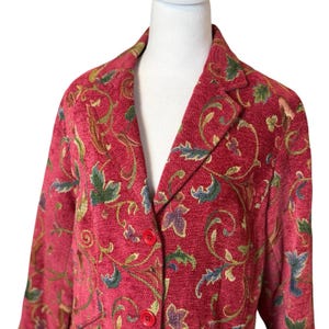 May include: A red blazer with a floral pattern in green, blue, and gold. The blazer has a notched collar and red buttons. The fabric has a textured appearance.
