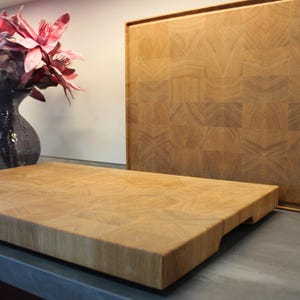 Op de afbeelding: Twee houten snijplanken met een rasterpatroon. De planken zijn gemaakt van lichtbruin hout en hebben een natuurlijke afwerking. De planken liggen op een grijs aanrecht.