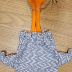 Puede incluir: Una bolsa de tela con un patr&oacute;n de chevr&oacute;n gris y blanco, con dos ap&eacute;ndices naranjas rellenos que sobresalen por la parte superior, asegurada con un cierre de cord&oacute;n y un trozo de cuerda atado alrededor de los elementos naranjas.