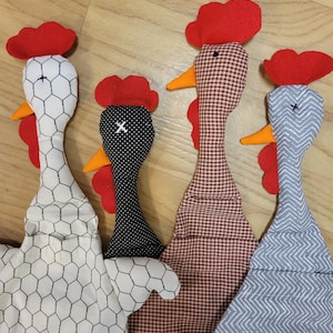 Puede incluir: Cuatro adornos de tela con forma de gallina con distintos patrones: blanco con estampado de malla de gallinero negra, negro con lunares blancos, cuadros vichy marrones y blancos, y gris con patr&oacute;n de chevr&oacute;n blanco. Cada uno tiene cresta y barbillas de fieltro rojo.