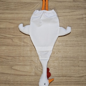 Puede incluir: Una bolsa de tela blanca con forma de pollo y una abertura el&aacute;stica en la parte superior. La bolsa presenta patas naranjas que sobresalen por arriba, una cabeza blanca con cresta y barbillas rojas, un pico naranja y una X negra bordada.