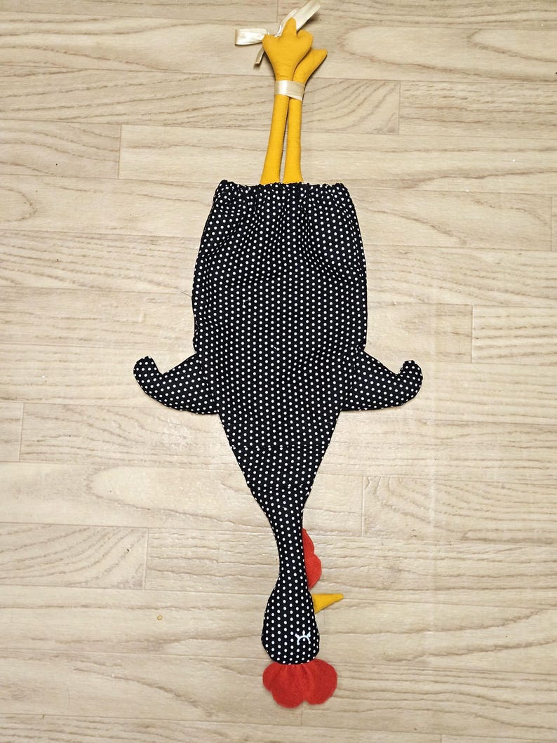 Puede incluir: Una bolsa de tela con forma de gallina sobre un fondo negro con lunares blancos. El dise&ntilde;o incluye patas amarillas atadas con una cinta color crema en la parte superior, una cresta y barbillas rojas, y un pico amarillo. El cuerpo tiene dos alas laterales.