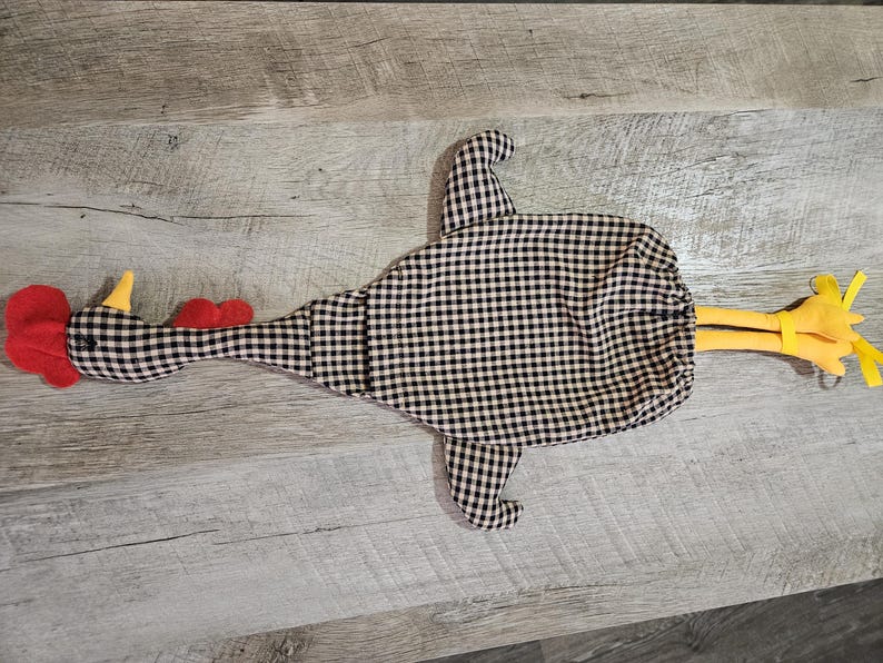 Puede incluir: Un accesorio de cocina de tela con forma de pollo y estampado de cuadros vichy en blanco y negro. La figura tiene una cresta y barbillas de fieltro rojo brillante, un pico amarillo y dos patas de fieltro amarillo en la parte trasera.