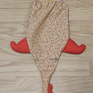 Puede incluir: Una bolsa de tela con forma de gallina con un cuerpo de color crema que presenta un peque&ntilde;o estampado floral rojo y azul. Tiene dos patas de tela amarilla en la parte superior, alas rojas en los lados, y una cresta roja y un pico amarillo.