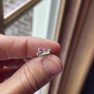 May include: Silver charm with the word "Slut" written in cursive.