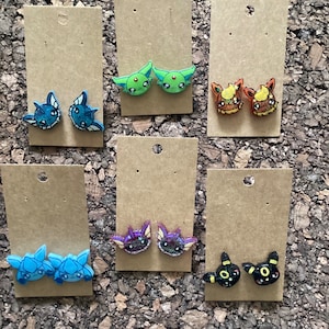 Può includere: Sei paia di orecchini colorati con personaggi Pokemon, esposti su cartoncino marrone. Gli orecchini sono realizzati in resina e presentano una varietà di personaggi Pokemon, tra cui Eevee, Vaporeon, Jolteon, Flareon, Espeon e Umbreon.