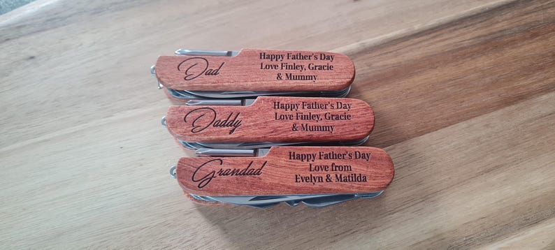 May include: Three personalized wooden pocket knives with stainless steel tools. Each knife is engraved with a different name: "Dad", "Daddy", and "Grandad". The knives also feature the text "Happy Father's Day" and a personalized message.