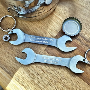Può includere: Due apribottiglie argentati a forma di chiave inglese con portachiavi e testo inciso. Uno dice "To Dad, Happy Father's Day Love, Jacob & Holly xx". L'altro dice "If Dad can't fix it no one can."