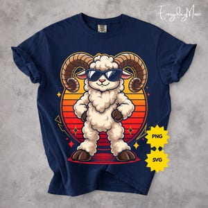 May include: Navy blue t-shirt featuring a cartoon ram wearing sunglasses, set against a sunset-colored circle. The ram has large, curved horns and is standing with its arms at its sides. The shirt has rolled-up sleeves.