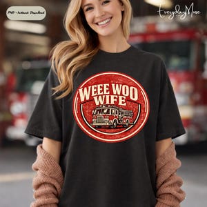 May include: Black t-shirt with a distressed red and cream graphic. The graphic features a fire engine and the words "WEEE WOO WIFE" in a circular design. The shirt is a casual style.