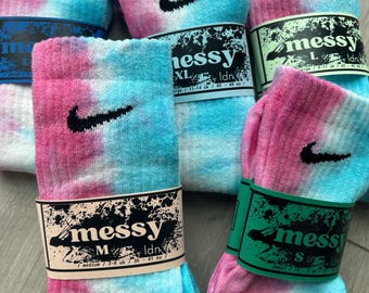 May include: Four pairs of tie-dye socks with a Nike swoosh logo. The socks are in different sizes: small, medium, large, and extra large. Each sock has a tag with the word "messy" and the size.