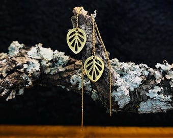 May include: A pair of gold-tone threader earrings featuring delicate, flat, leaf-shaped charms with a cut-out vein pattern. Each earring consists of a thin chain that passes through the ear, ending in a straight, slender metal post.