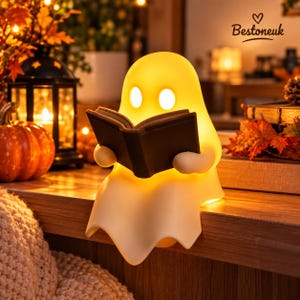 May include: A glowing, off-white, ghost-shaped lamp reading a dark-colored book. The lamp features two oval-shaped eye cutouts and emits a warm, soft light. The text "Bestoneuk" with a heart icon is visible in the upper right corner.