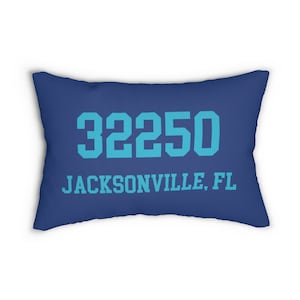 May include: A rectangular blue pillow with the text "32250 JACKSONVILLE, FL" printed in a lighter shade of blue. The pillow is a solid color with a simple, clean design.