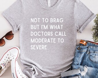 May include: Gray t-shirt with the text "Not to brag but I'm what doctors call moderate to severe" printed in white.