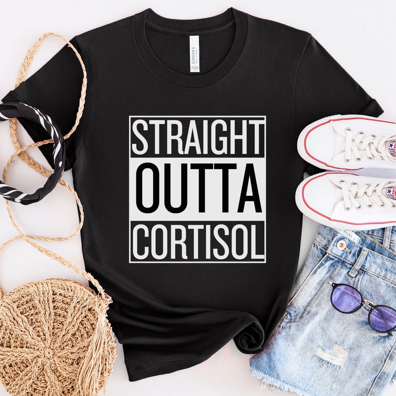 May include: Black t-shirt with the text "STRAIGHT OUTTA CORTISOL" in a white, bold font. The shirt is displayed with white sneakers, denim shorts, and accessories.