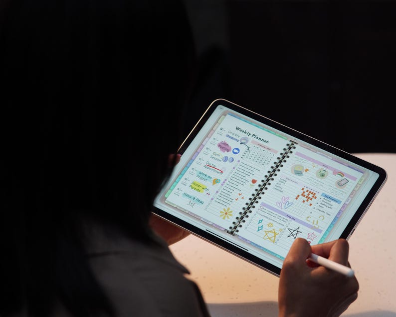 May include: A digital tablet displaying a weekly planner with colorful illustrations and handwritten notes. The tablet is held by a person, with a stylus in hand. The planner features sections for appointments, to-do lists, and notes.