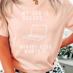 Peut inclure: Un t-shirt rose avec le texte "Mon travail est sécurisé... Personne d'autre ne le veut" et un dessin d'un ordinateur portable.