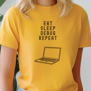 Könnte beinhalten: Gelbes T-Shirt mit einer schwarzen Grafik eines Laptops und dem Text "Eat Sleep Debug Repeat".
