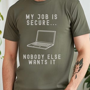 Peut inclure: Un t-shirt vert avec le texte "Mon travail est sécurisé... Personne d'autre ne le veut" et un dessin d'un ordinateur portable.