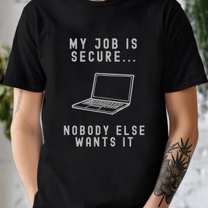 Peut inclure: Un t-shirt noir avec du texte blanc qui dit "Mon travail est sécurisé... Personne d'autre ne le veut". Le t-shirt présente également un dessin simple d'un ordinateur portable.