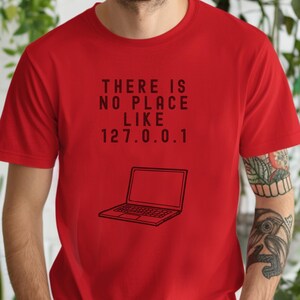 Puede incluir: Camiseta roja con un gráfico negro que dice "There is no place like 127.0.0.1" y una ilustración de un portátil.
