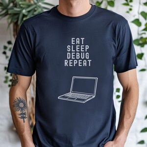 Pode incluir: Uma camiseta azul marinho com um gráfico branco de um laptop e o texto "Eat Sleep Debug Repeat".