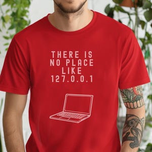 Può includere: Maglietta rossa con testo bianco che recita "There is no place like 127.0.0.1" e un contorno bianco di un computer portatile.