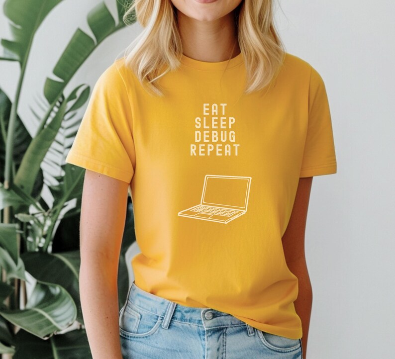 May include: Mustard yellow t-shirt with the text "EAT SLEEP DEBUG REPEAT" and a line drawing of a laptop. The shirt is paired with blue jeans. The overall theme is tech and coding.