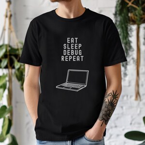 May include: Black t-shirt with the text "EAT SLEEP DEBUG REPEAT" in white, along with a white line drawing of a laptop. The shirt is a crew neck and has short sleeves.