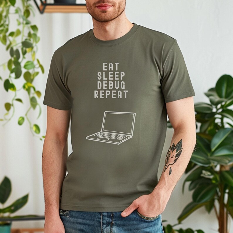 May include: Olive green t-shirt with the text "EAT SLEEP DEBUG REPEAT" and a laptop graphic in white. The shirt is a short-sleeved crew neck.