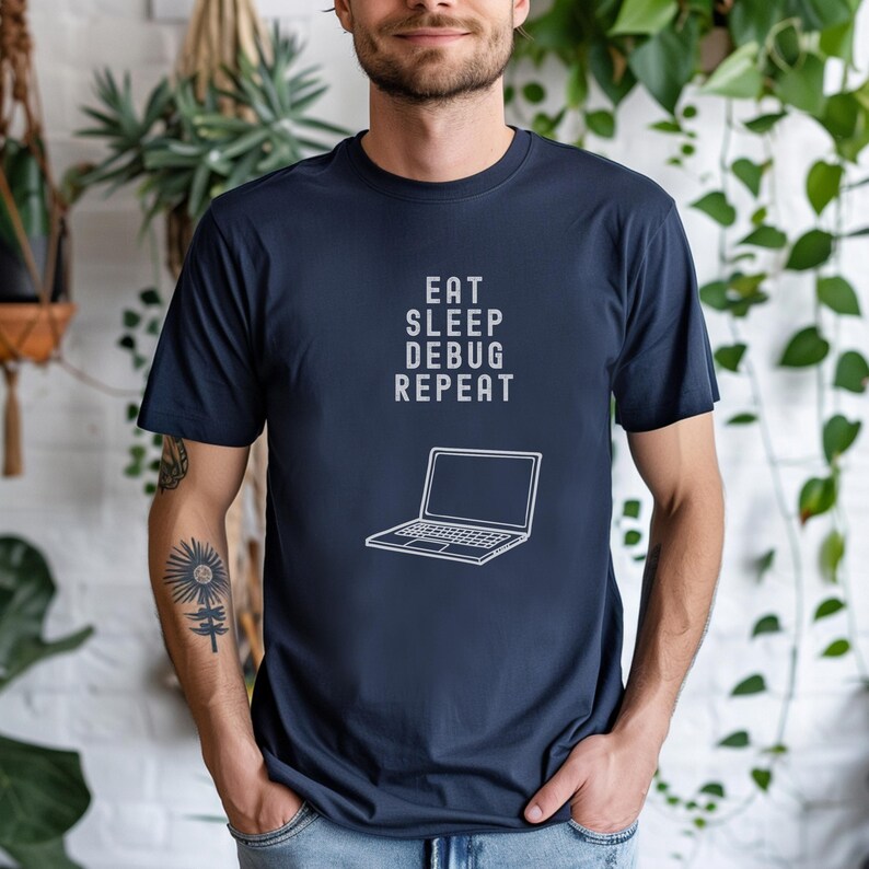 May include: Navy blue t-shirt with the text "EAT SLEEP DEBUG REPEAT" above a white outline of a laptop. The shirt is a short-sleeved crew neck.
