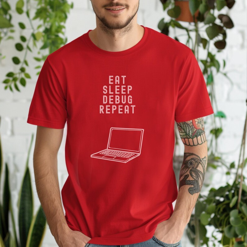 May include: A red t-shirt with the words "EAT SLEEP DEBUG REPEAT" printed in white, along with a white outline of a laptop. The shirt is short-sleeved and made of a soft material.